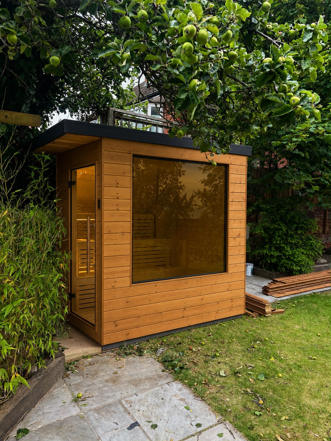 Traditional wood 3-5 man outdoor sauna with tinted glass window in a garden